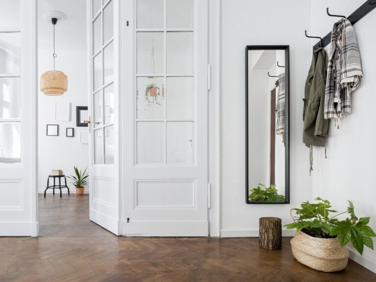 White hallway with coat hooks and full-length mirror, cozy and minimalistic interior design.