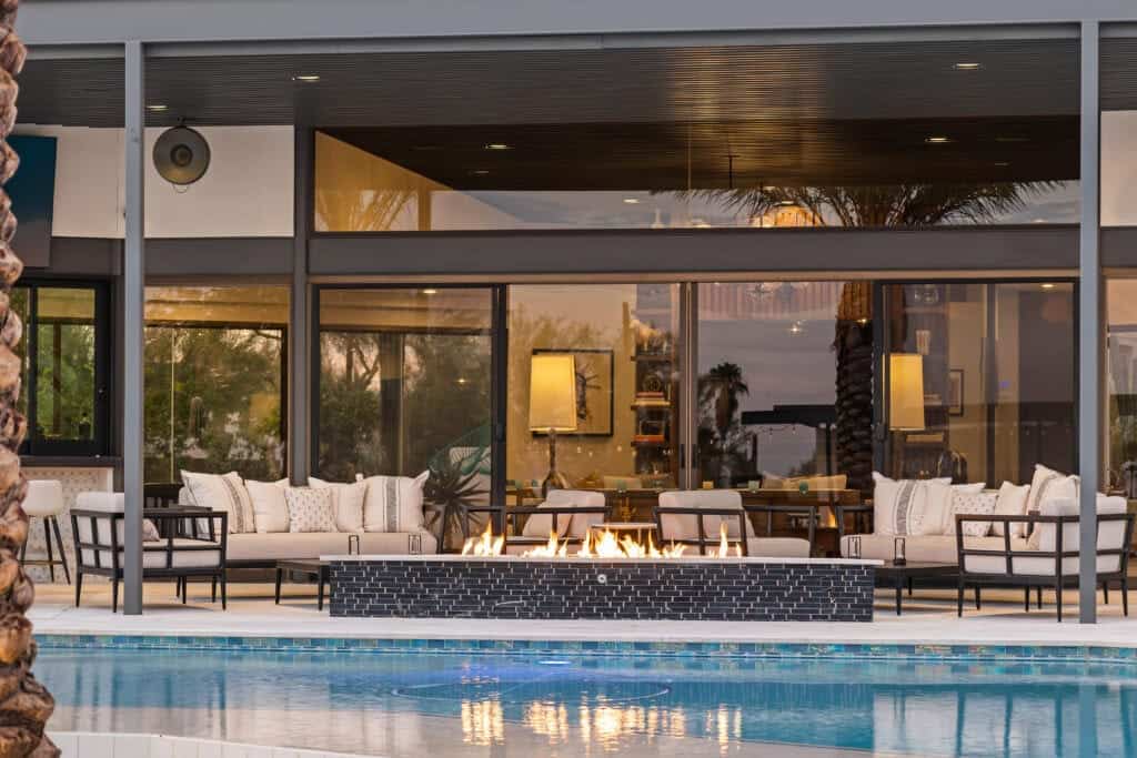 Modern outdoor lounge area setup by Meredith Lane with fireplace overlooking pool and sunset view.