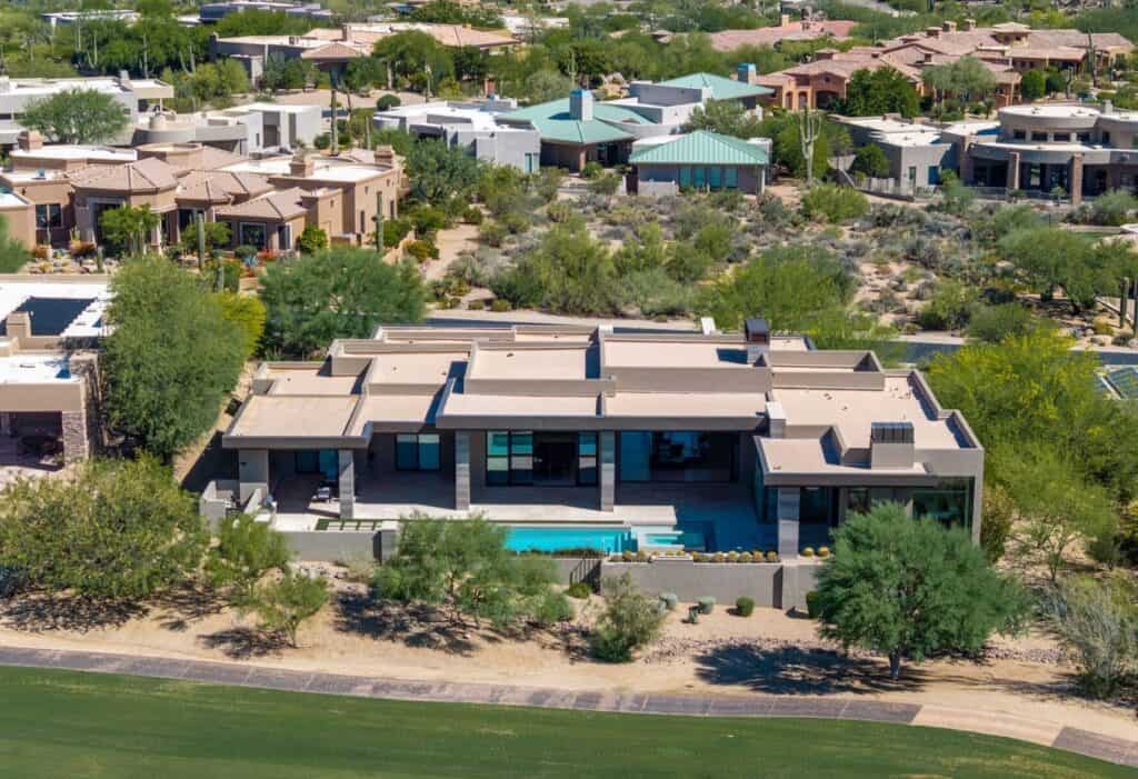 Aerial view of contemporary desert home with pool, surrounded by desert plants and neighboring stylish houses.