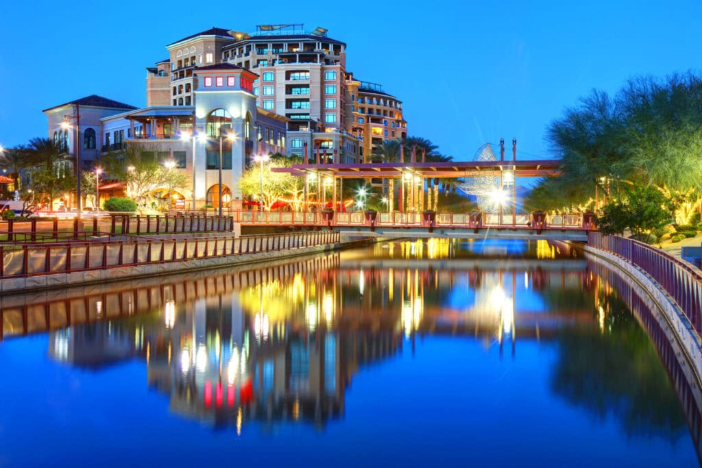 Luxurious apartment building in Scottsdale with water feature and vibrant evening lights.