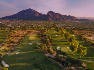 Scenic view of a golf course with mountains in the background at sunset.