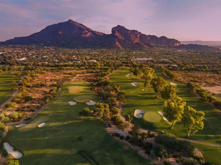 Scenic view of a golf course with mountains in the background at sunset.